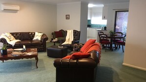 A living room with a brown leather sofa, a coffee table, and a dining area with a table and chairs. - Bird Abode Accommodation in central Maryborough (Maryborough)