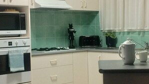A kitchen with white cabinets, a microwave, a stove, a toaster, and a kettle on the counter. - Bird Abode Accommodation in central Maryborough (Maryborough)