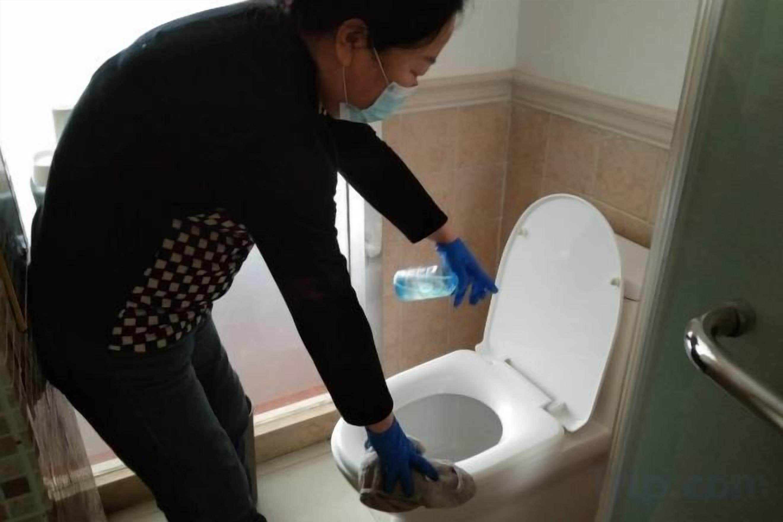 A person cleaning a toilet with a spray bottle.