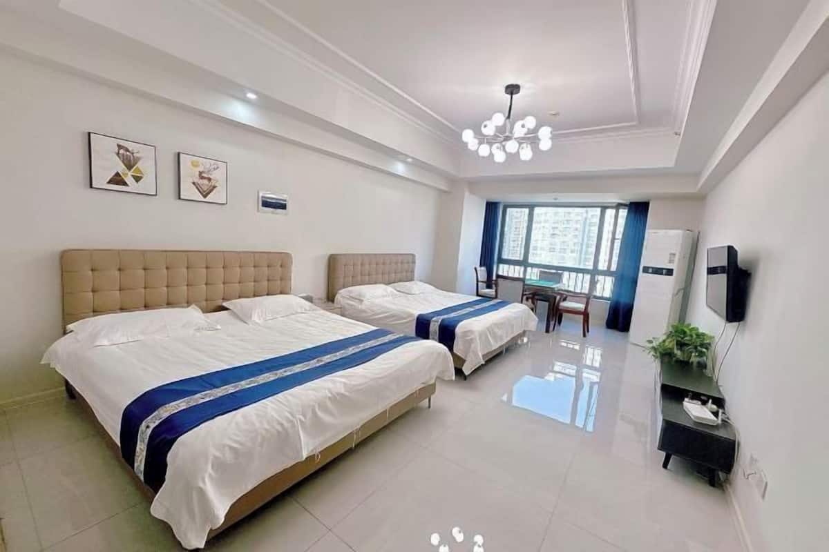 Quarto de hotel com duas camas, uma mesa, uma cadeira, uma televisão e uma janela com vista para edifícios.