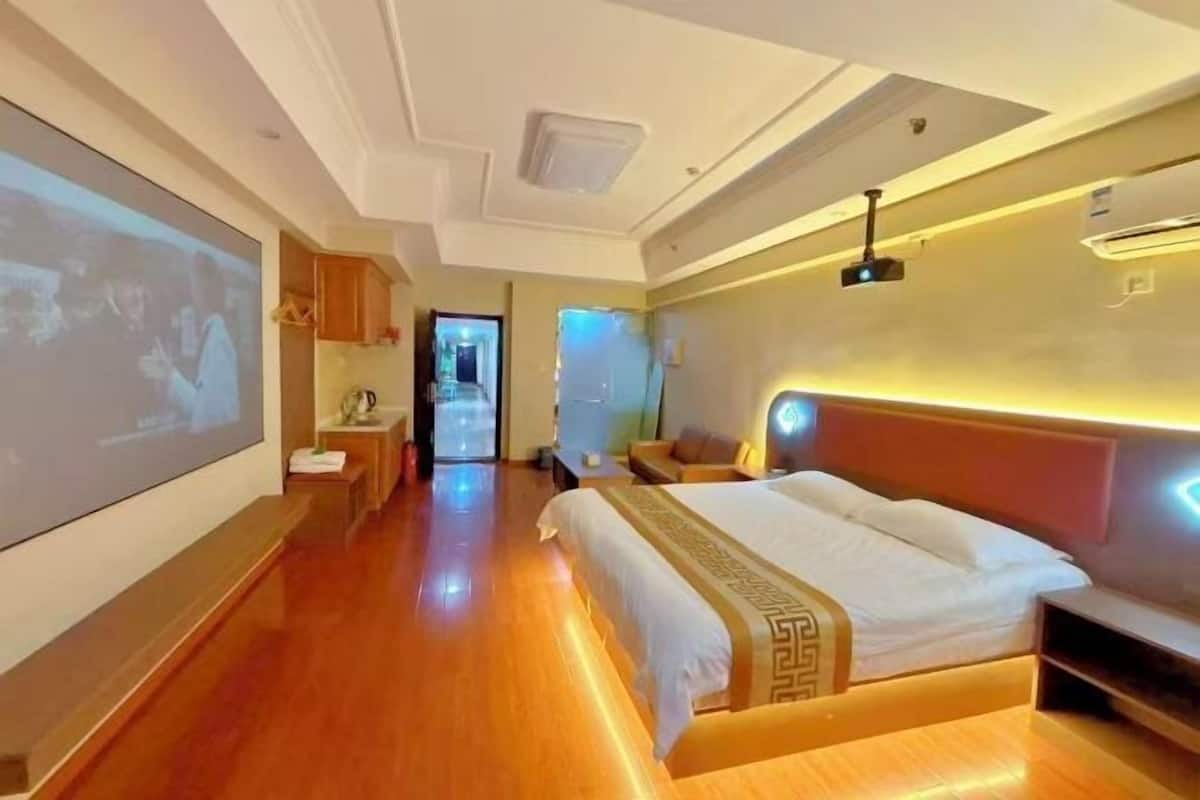Quarto de hotel com uma cama grande, televisão, piso de madeira e teto com iluminação embutida.