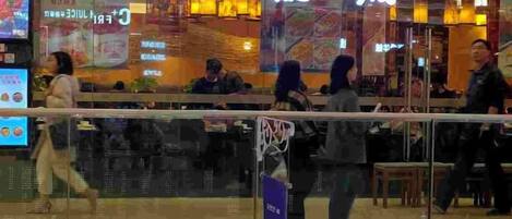 A restaurant with a glass barrier in front, people inside, and a digital menu display outside.