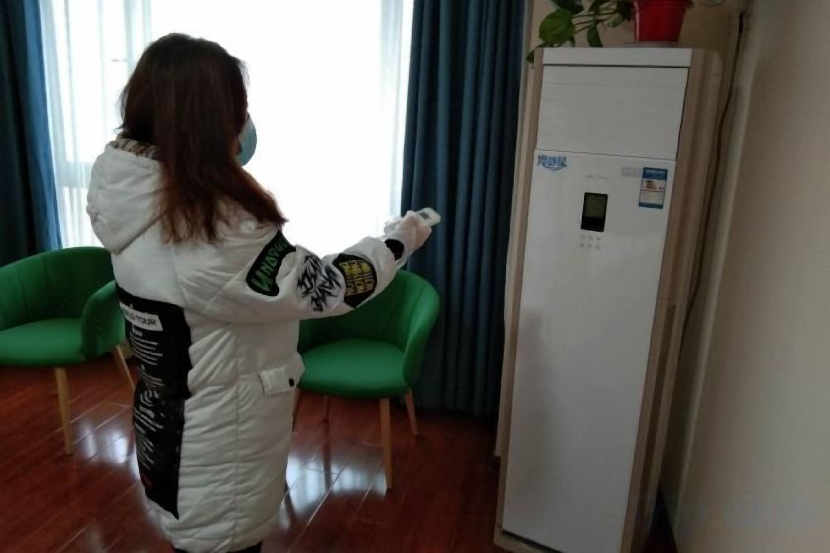 Una persona con bata blanca interactuando con una pizarra en una habitación con sillas verdes y un refrigerador.