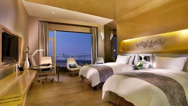 Une chambre d’hôtel moderne équipée de deux lits, d’un bureau, d’une chaise et d’une grande fenêtre donnant sur la ville.