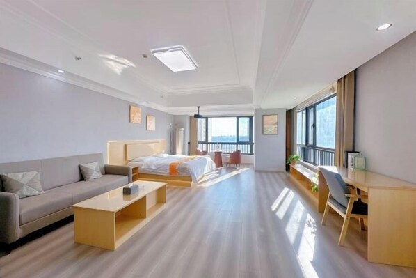 A modern hotel room with a bed, sofa, desk, and large windows. - Yiyi Sentiment Apartment Hotel (Bengbu)