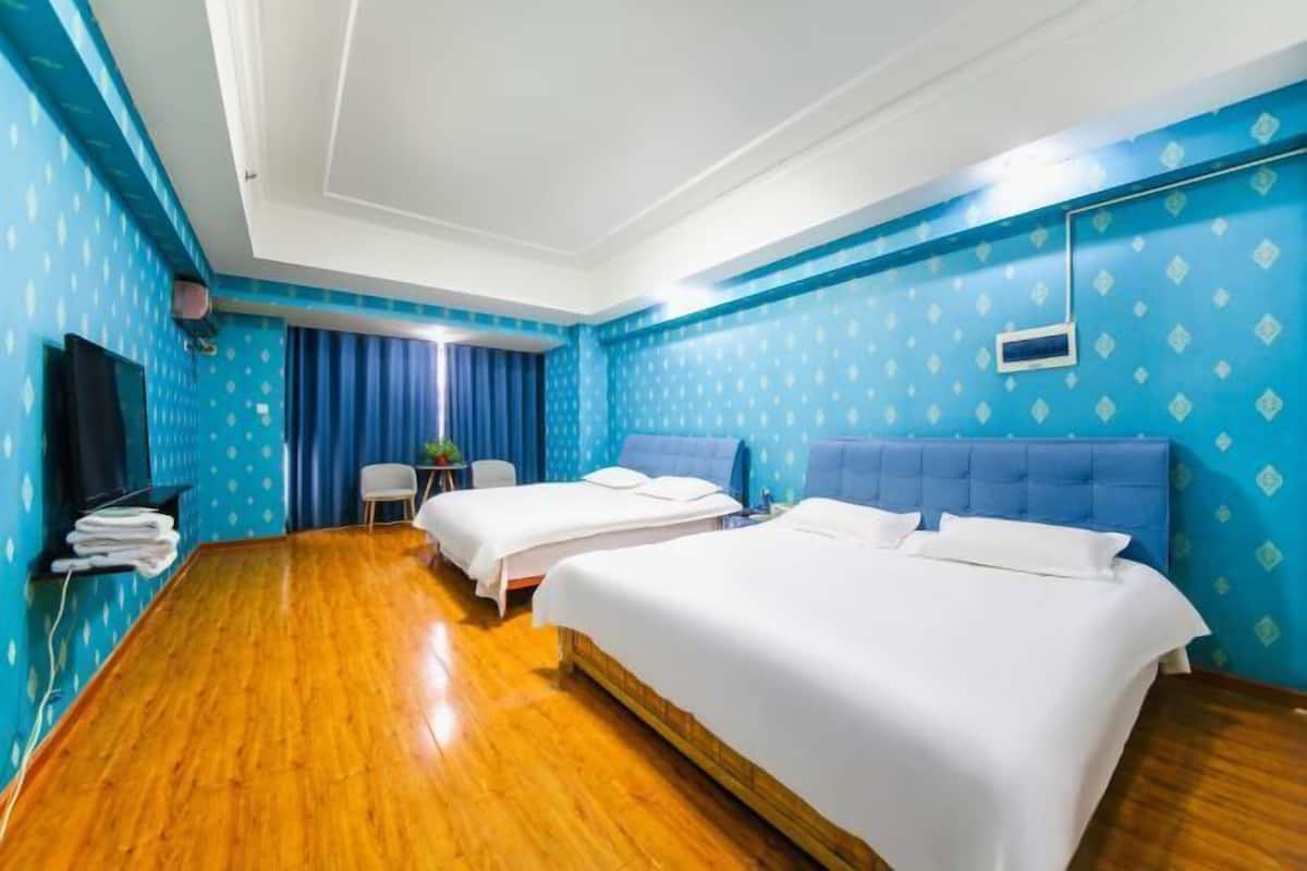 Quarto de hotel com duas camas, piso de madeira, televisão e escrivaninha com cadeira.
