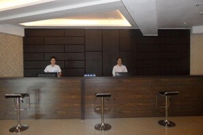 Una reception con due membri dello staff, un banco di legno e tre sgabelli in metallo.