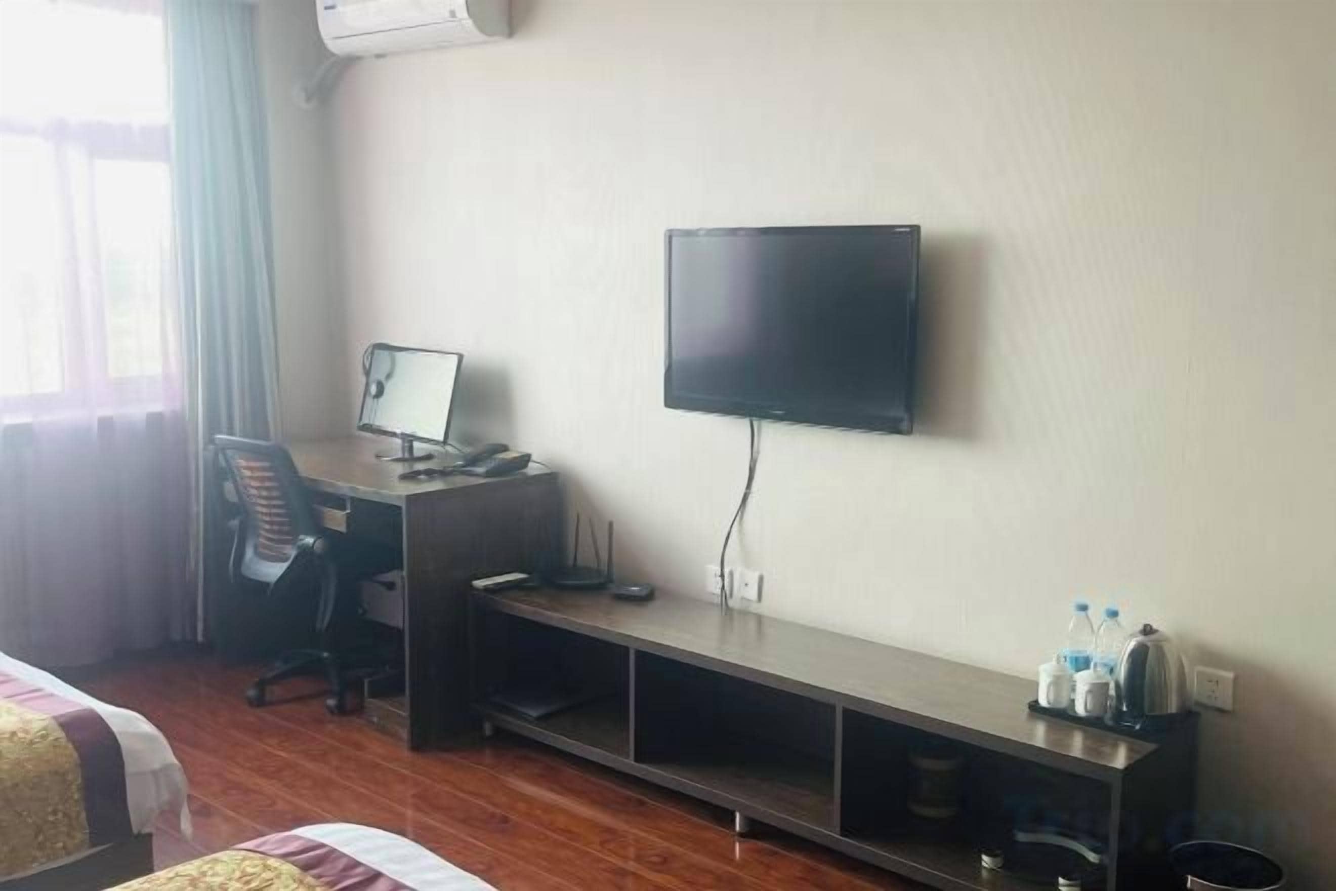 A hotel room with a bed, a desk with a computer, a television, and a shelf with water bottles.