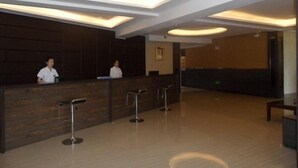 A reception area with a wooden reception desk, two receptionists, and a waiting area with metal stools. - Wanda Motel (Bei'an)
