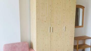 Una habitación con armario, espejo y una pequeña estantería de madera.