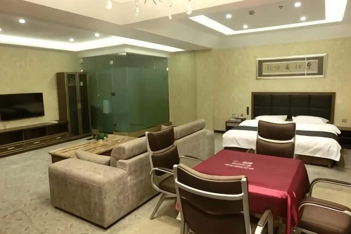Ein Hotelzimmer mit Sofa, Esstisch, Fernseher, Bett und einer grüngläsernen Trennwand.