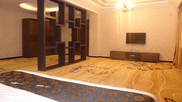 A hotel room with a large bed, a TV mounted on the wall, and a wooden partition. - Wanda Motel (Bei'an)