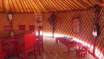 Interior de una yurta tradicional, con una mesa redonda, sillas rojas y una pared con motivos decorativos.