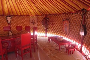 A traditional yurt interior with a round table, red chairs, and a patterned wall.