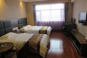 A hotel room with two beds, a TV, a desk, and a window with curtains.
