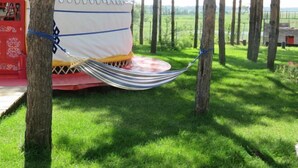 A tent with a striped hammock hanging from it, surrounded by trees and grass. - Wanda Motel (Bei'an)