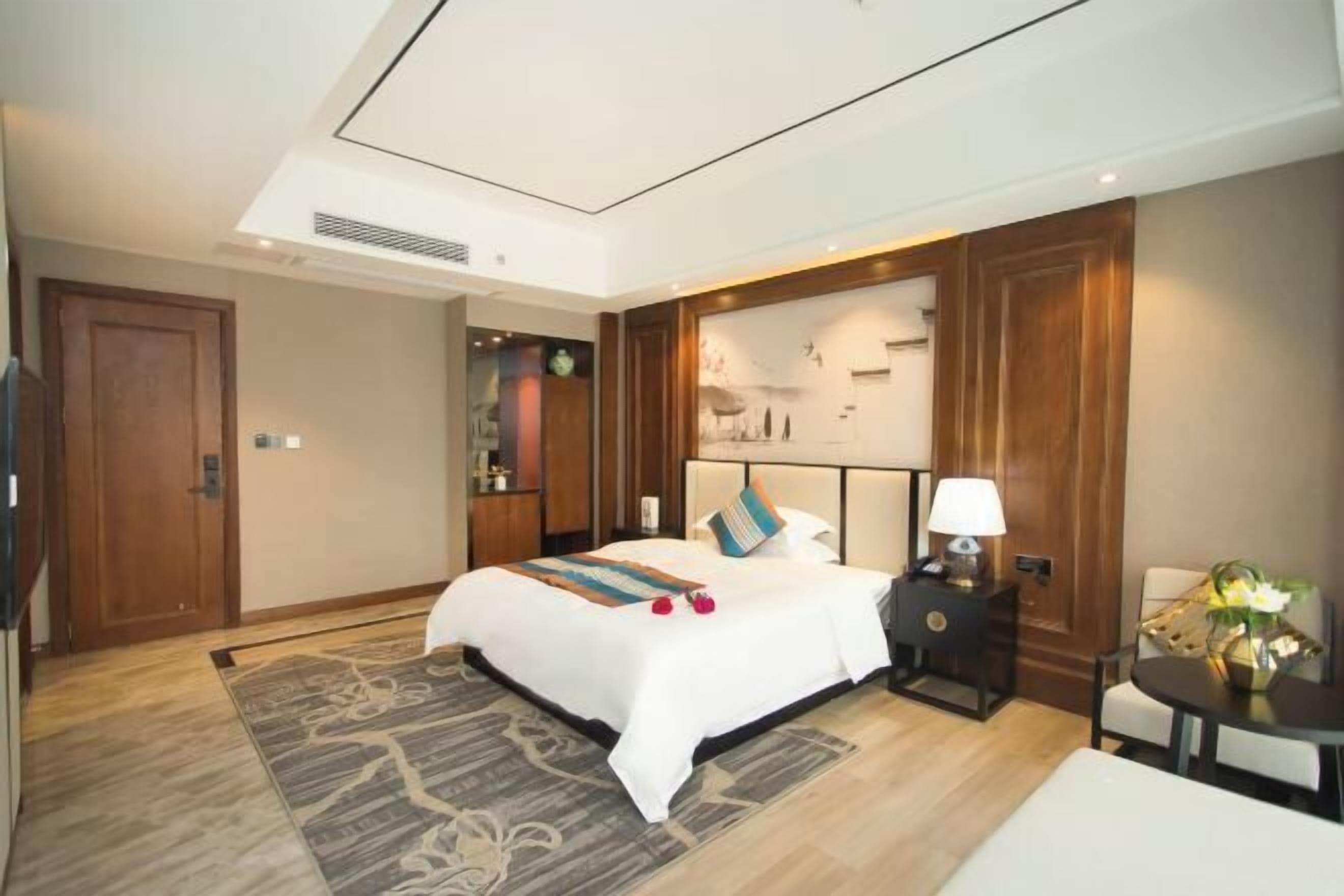 Hotelkamer met een groot bed, een nachtkastje met een lamp, een klein tafeltje met een vaas en een decoratief wandpaneel.