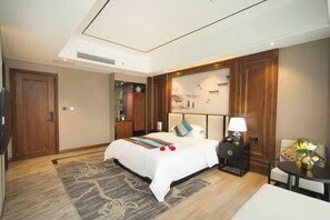A hotel room with a large bed, a bedside table with a lamp, a small table with a vase, and a decorative wall panel. - Colorful Xiangxi Inn (Zhangjiajie)
