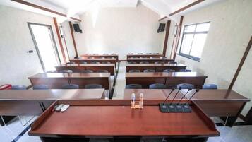 Un salón de conferencias con varias mesas y sillas, equipado con micrófonos y un proyector.