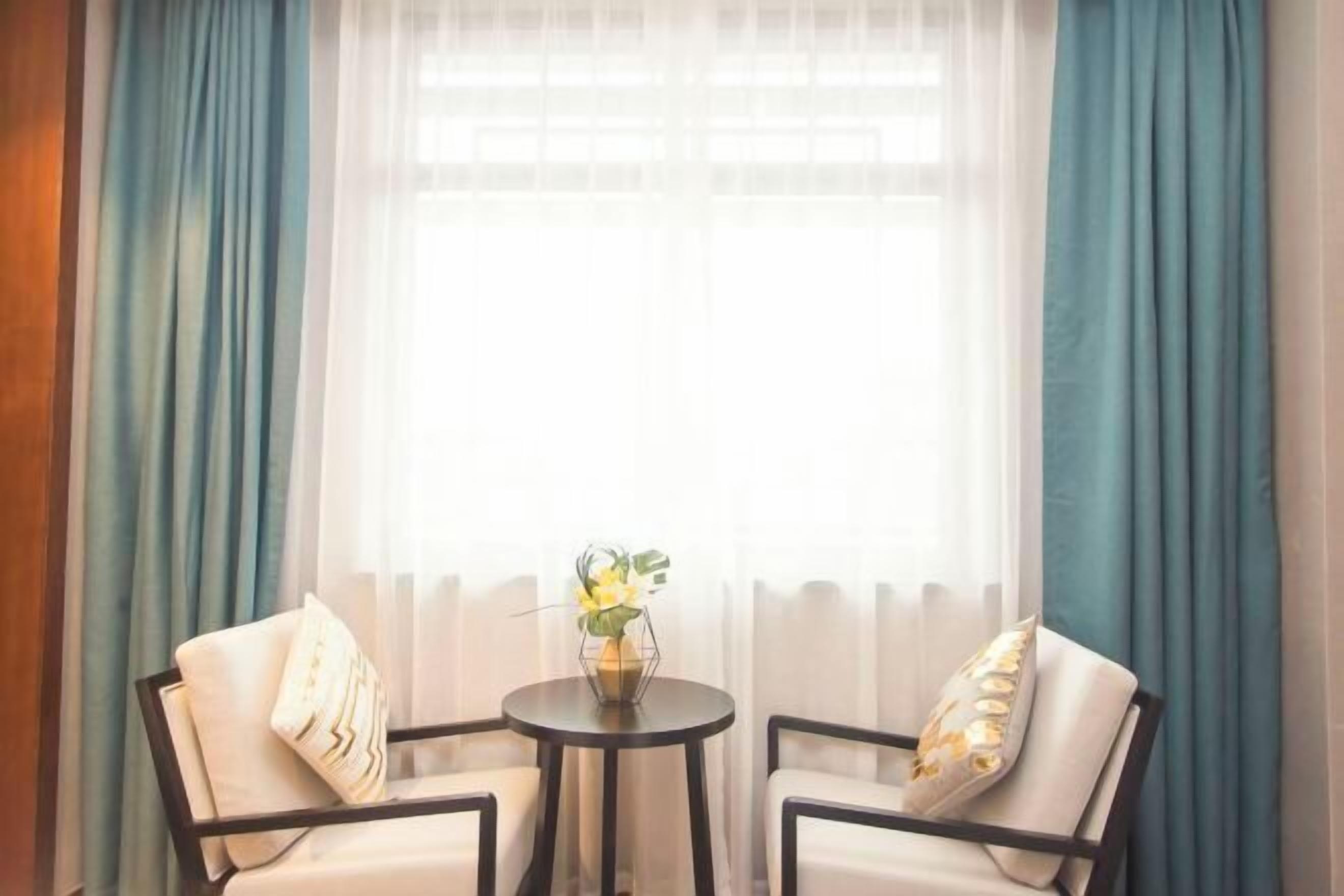 Een kamer met twee stoelen, een kleine tafel met een bloevas en een raam met gordijnen.