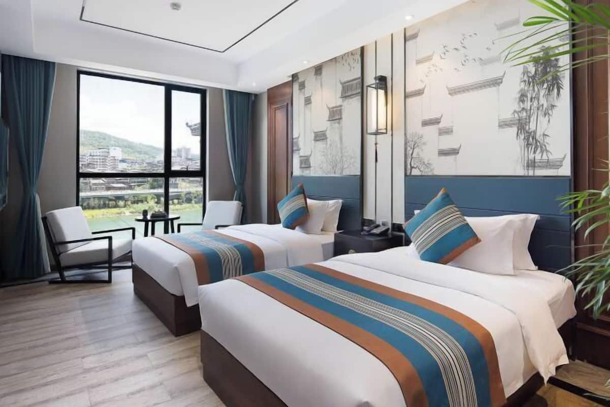 A hotel room with two beds, a view of the city, a desk, and a chair.