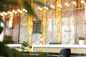 Un mostrador de recepción de hotel con encimera de mármol, una silla negra y un panel informativo fijado a la pared.
