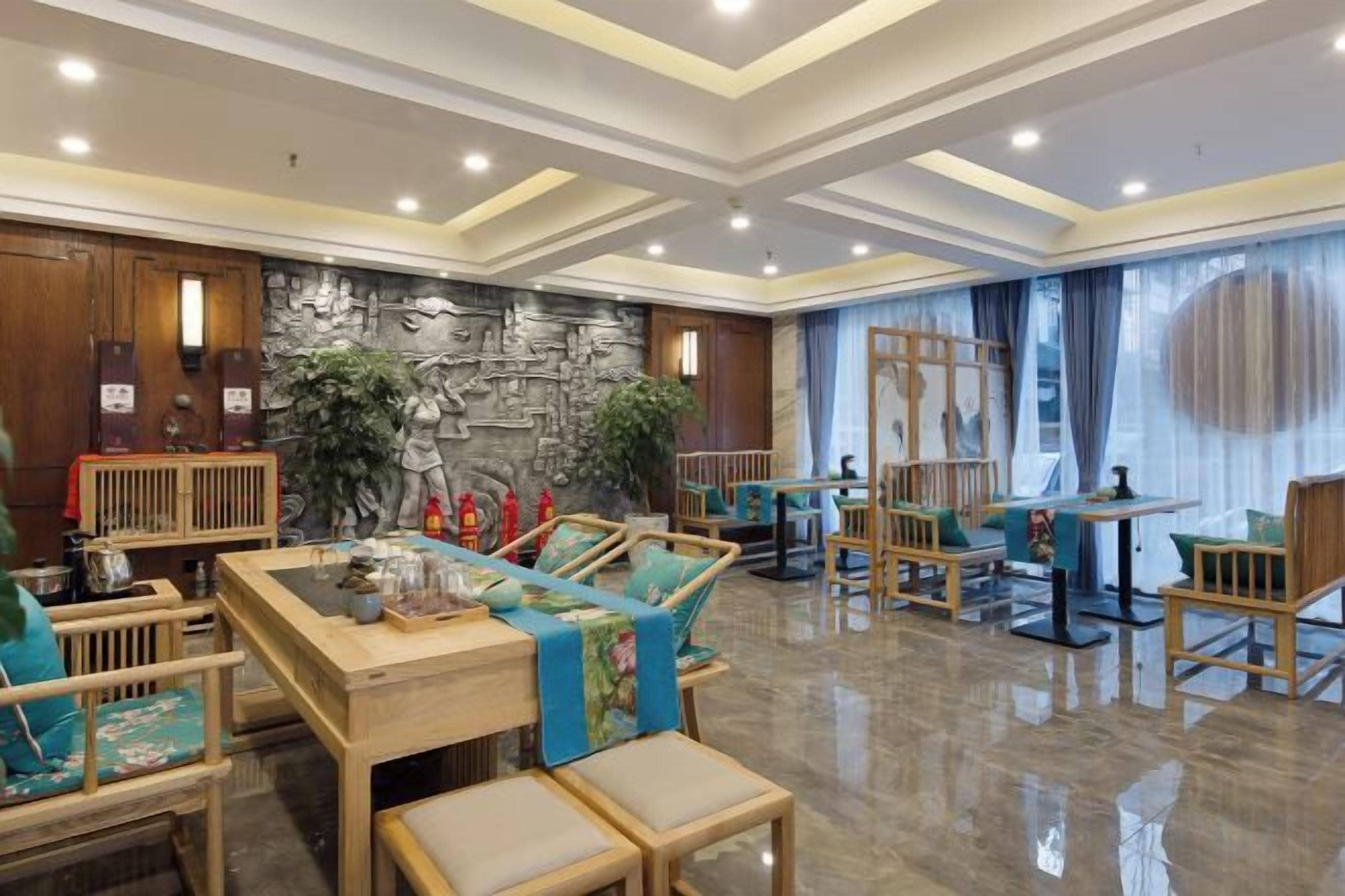 Un vestíbulo amplio con un mostrador de recepción de madera, zona de estar con sillas y sofás, un muro decorativo y un ventanal con cortinas.