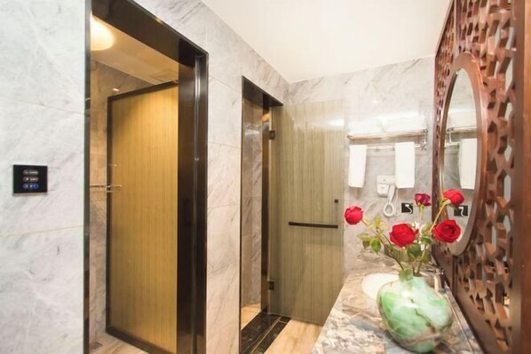 A modern bathroom with marble walls, a wooden door, and a sink with a vase of red roses. - Colorful Xiangxi Inn (Zhangjiajie)