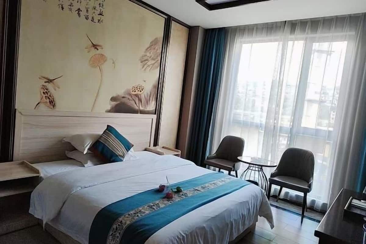A hotel room with a large bed, a desk, a chair, and a view of the city through the window.
