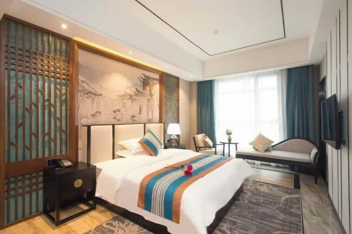 A hotel room with a bed, bedside tables, a TV, a sofa, and a decorative wall.