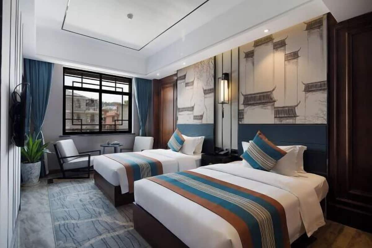 A hotel room with two beds, a sitting area, a large window, and traditional wall art.