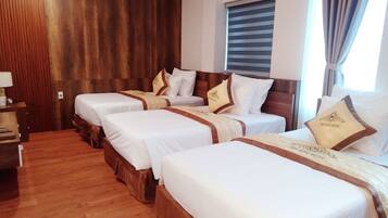 A hotel room with four single beds, wooden paneling on the walls, a window with blinds, and a nightstand with a lamp.