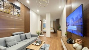 A modern living room with a grey sofa, a wooden coffee table, and a flat-screen TV mounted on the wall. - The King Hotel condotel Thai Nguyen (Phan Dinh Phung)
