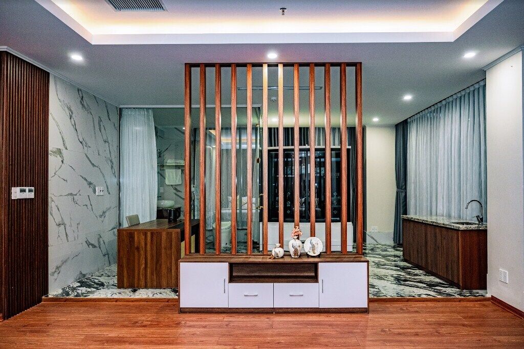 Una sala de estar moderna con una unidad de entretenimiento de madera, paredes con diseño de mármol y una zona de cocina con lavamanos.