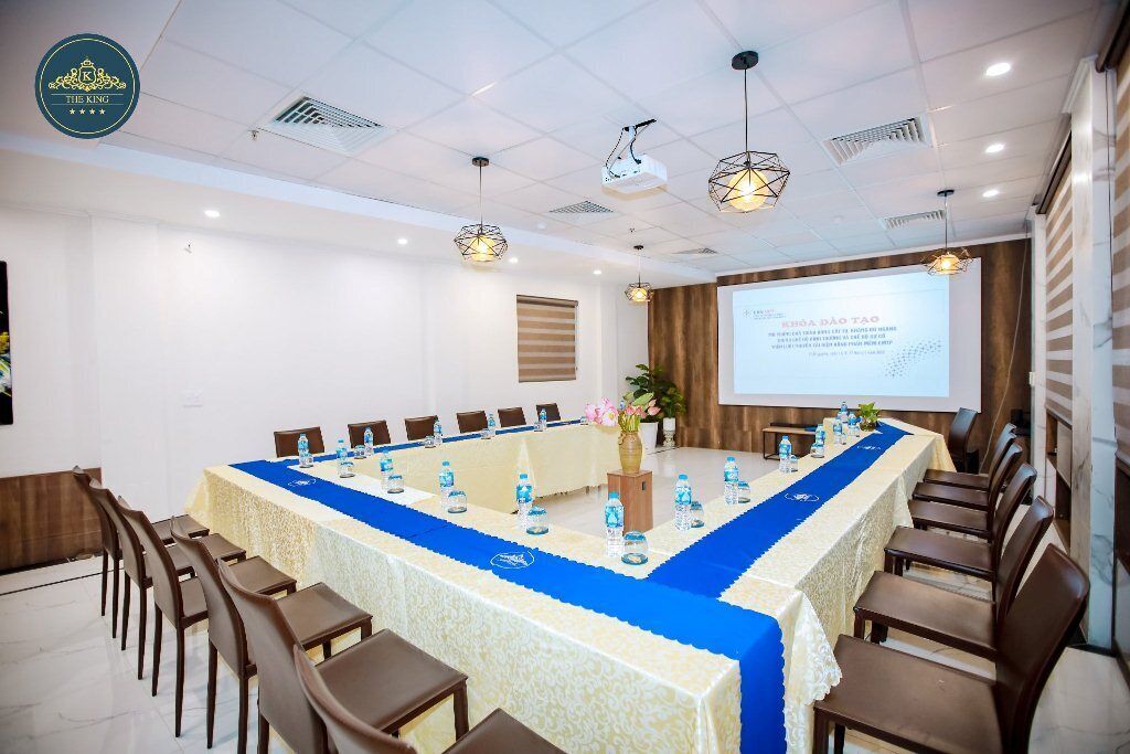 A conference room with a long table, chairs, a projector screen, and a floral arrangement.