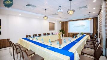 A conference room with a long table, chairs, a projector screen, and a floral arrangement.