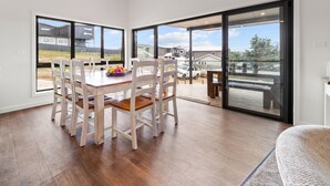 Un coin repas avec une table en bois et des chaises blanches, de grandes fenêtres et une vue sur un quartier résidentiel.