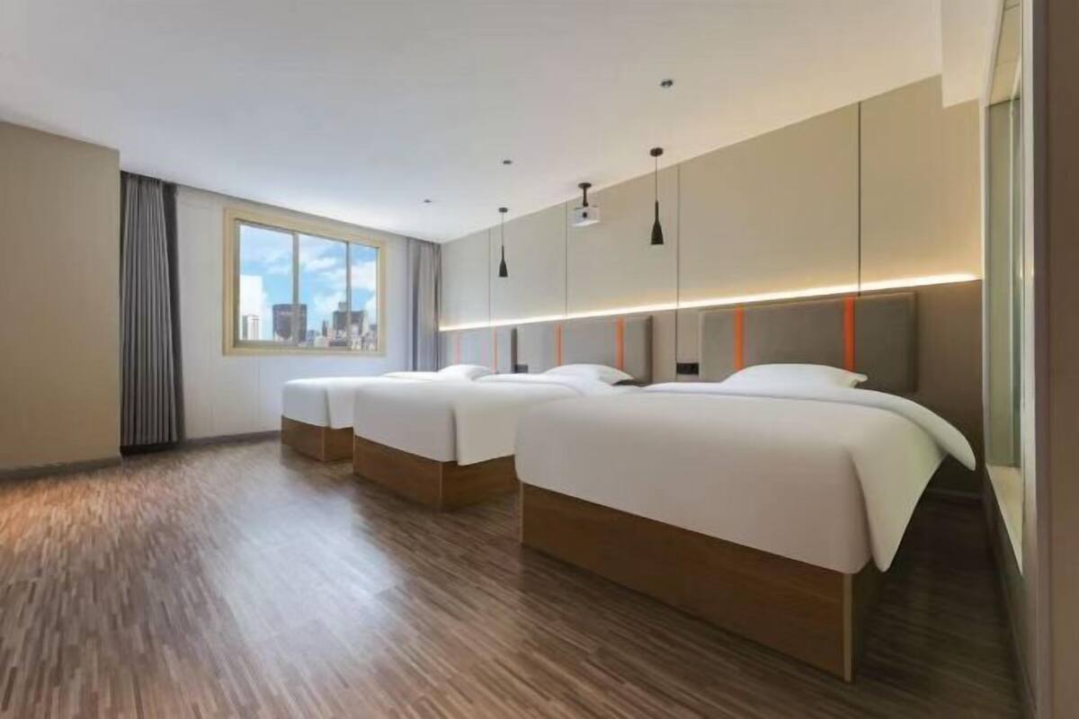 A hotel room with three beds, a large window, and a city view.