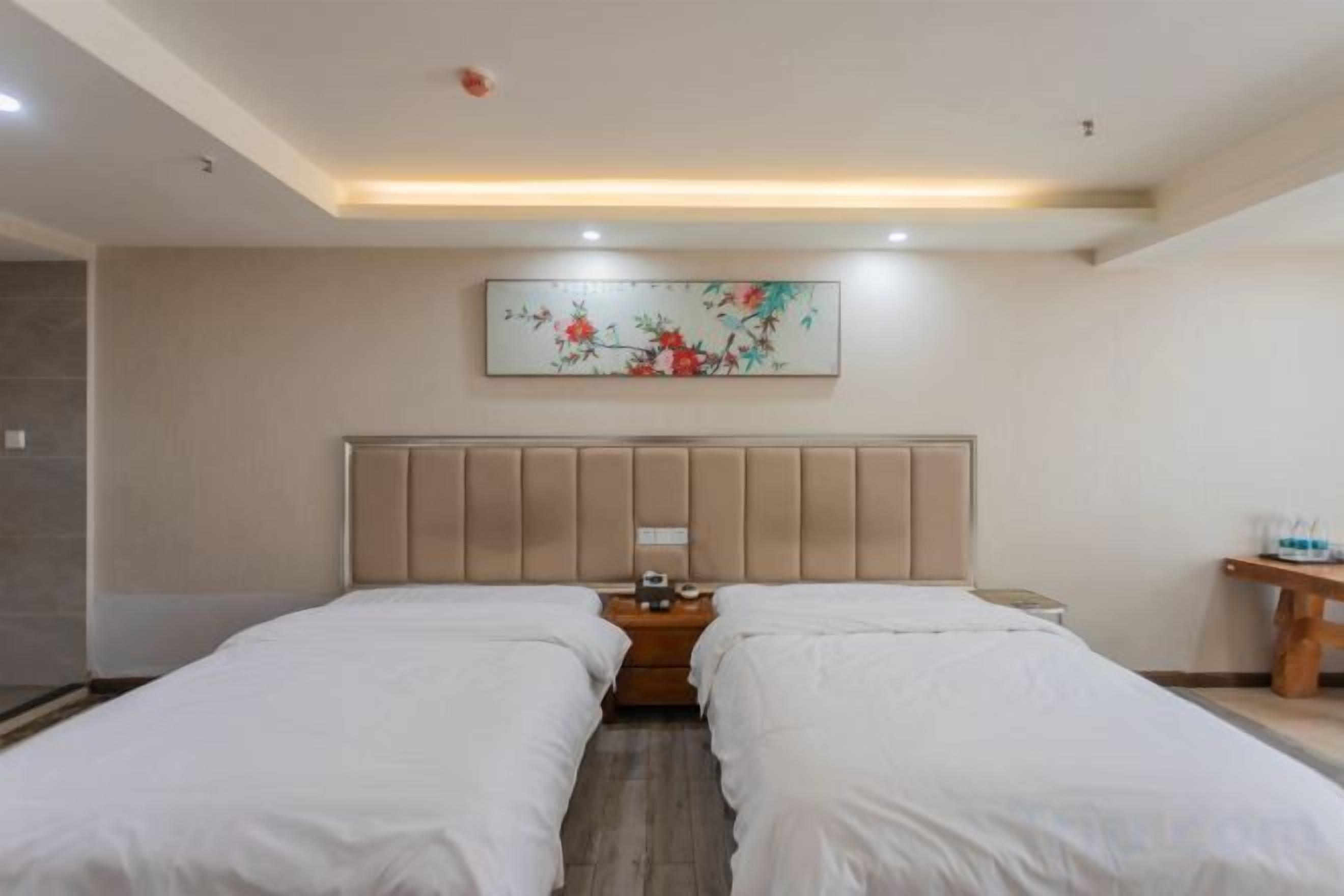 A hotel room with two beds, a headboard, a bedside table, and a wall-mounted artwork.