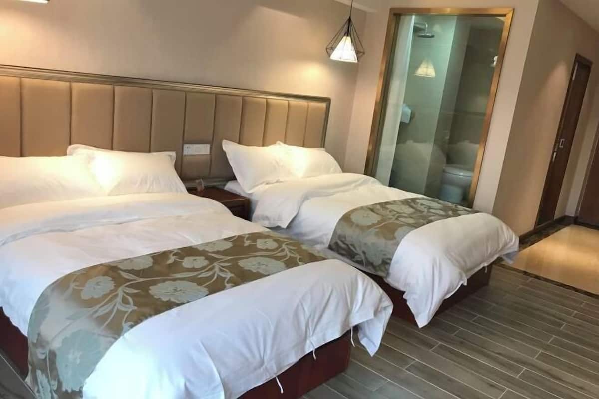 A hotel room with two beds, a large window, and a separate bathroom visible through a glass door.