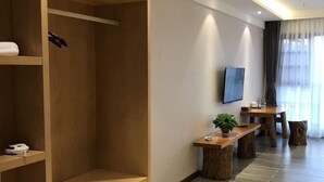 Ein modernes Hotelzimmer mit einem Holzschrank, einem kleinen Tisch mit einer Pflanze, einem an der Wand montierten Fernseher und einem Essbereich mit Holztisch und Stühlen.