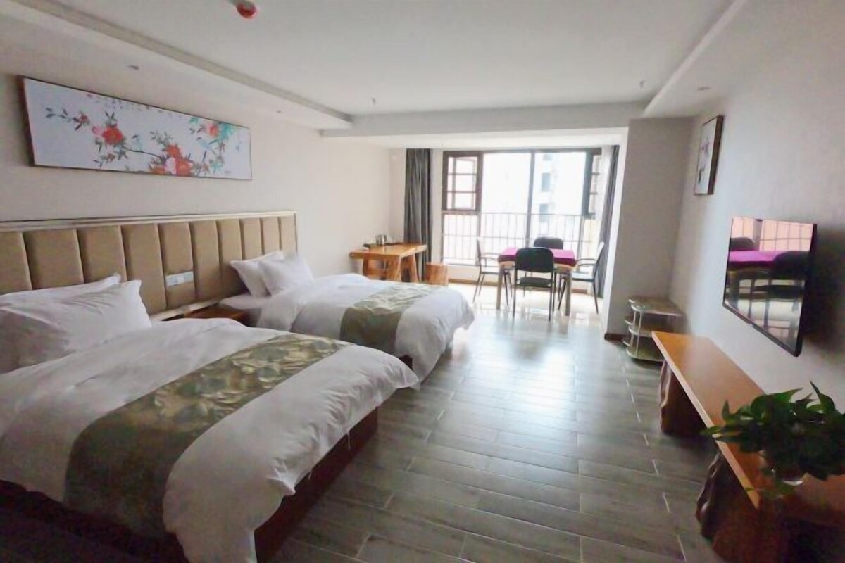 Habitación de hotel con dos camas, un escritorio, una silla, un televisor y un balcón.