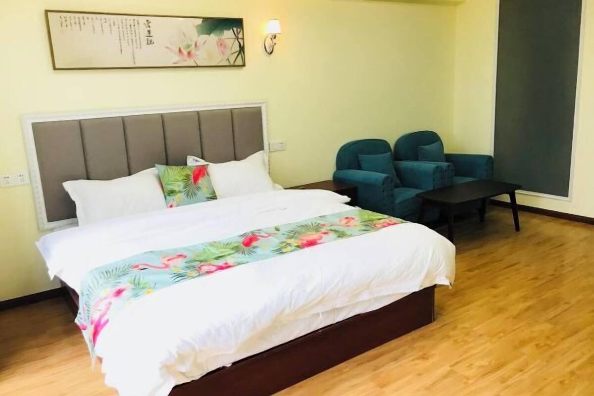 A hotel room with a bed, two chairs, a small table, and a wall-mounted artwork.