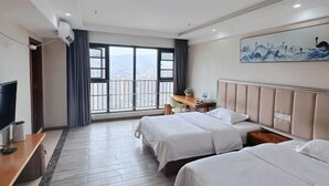 Ein Hotelzimmer mit zwei Betten, einem Schreibtisch, einem Fernseher und einem großen Fenster mit Blick auf die Stadt.