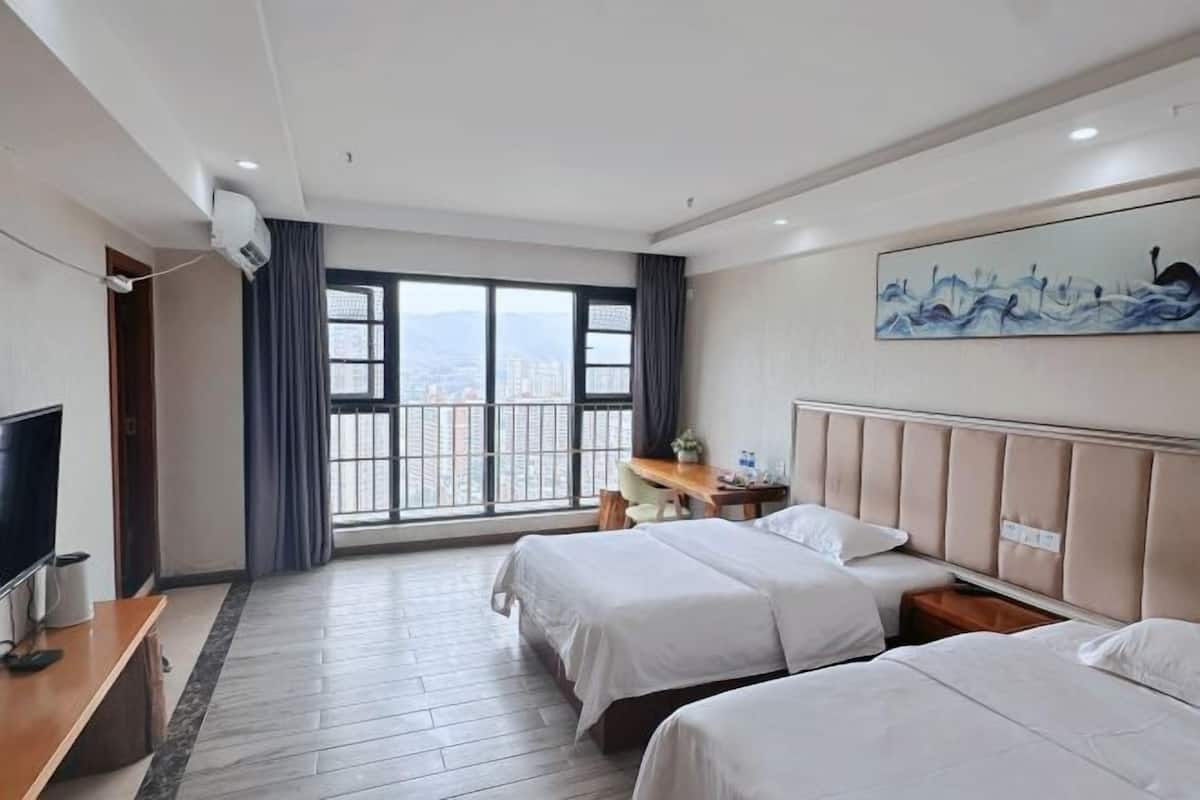 A hotel room with two beds, a desk, a TV, and a large window with a city view.