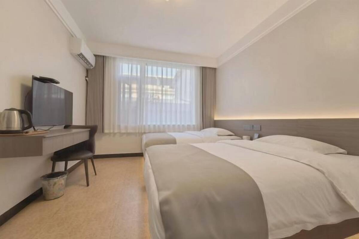 A hotel room with two beds, a desk with a television, a kettle, and a bucket.
