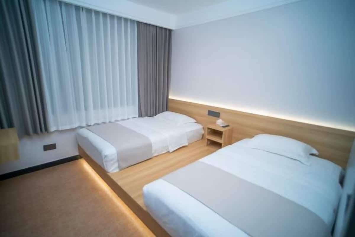 A hotel room with two beds, a nightstand, a lamp, and a window with curtains.