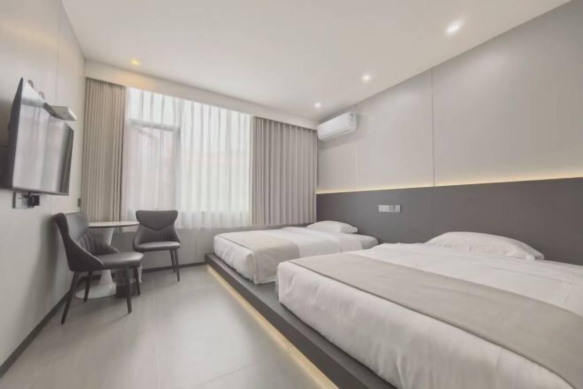 A modern hotel room with two beds, a desk, a chair, and a TV.