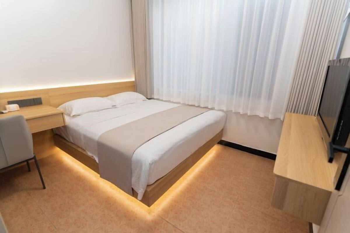 A modern hotel room with a bed, bedside table, chair, and a TV.