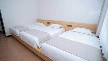 Habitación de hotel con tres camas individuales, cabecera de madera y pared blanca.